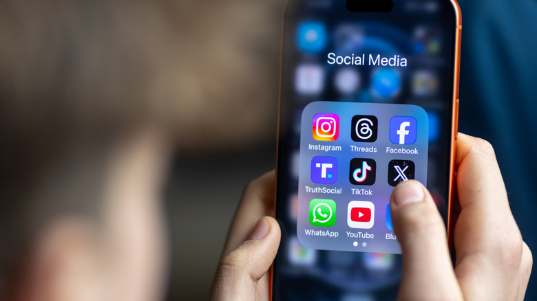 A teenager opens up a folder of social media apps on their iPhone.
