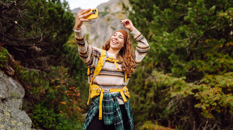 A woman takes a selfie with their phone while hiking through mountains.