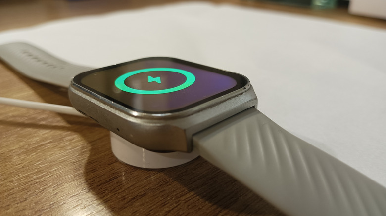 Close-up of a smartwatch with a silver band on a magnetic charger.