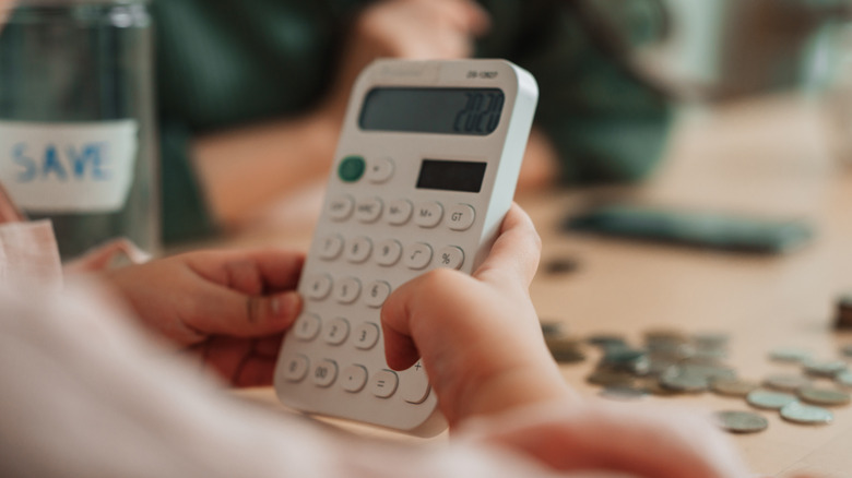 Close up of a calculator being held by a child counting coins with the help of an adult