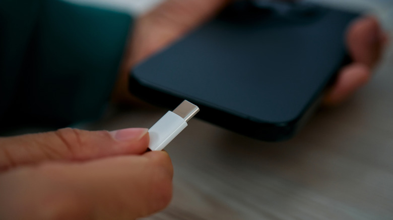 Someone holding a USB-C cable in one hand and a smartphone in the other.