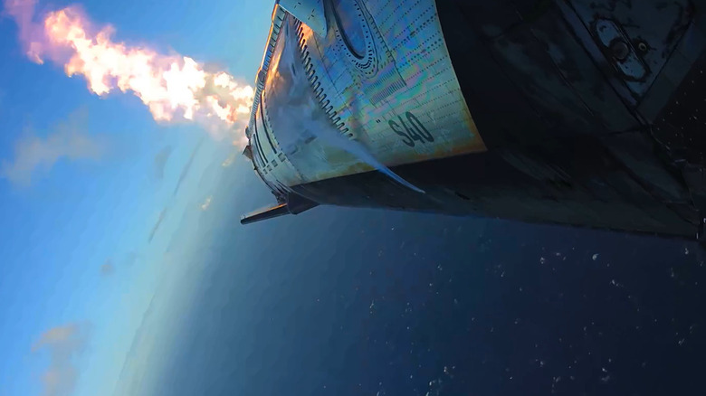 Starship seen on its side as it lights its Raptor engines for landing.