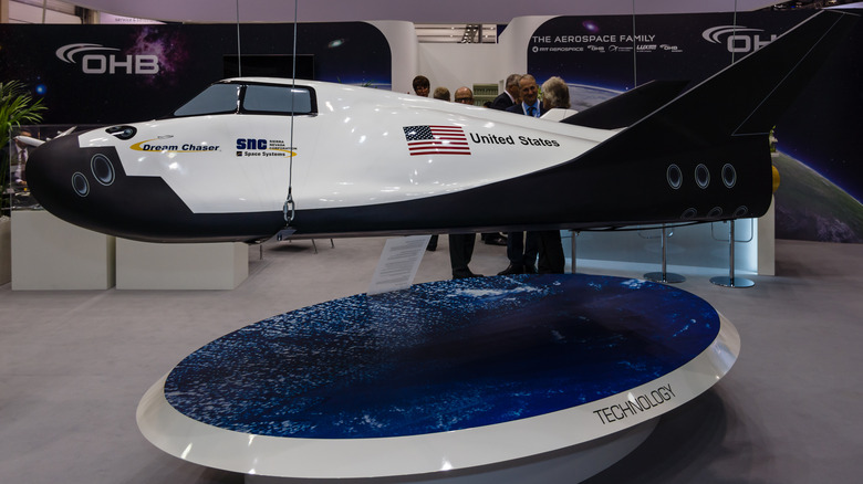 A model Dream Chaser Cargo System on display as people in suits stand around in conversation