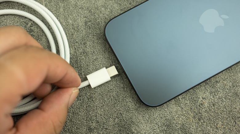 A hand about to place a USB-C cable into a black iPhone laying on a carpet