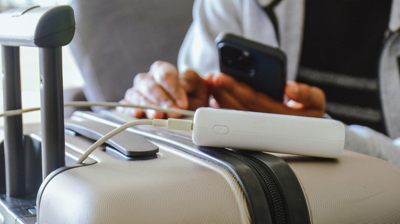 Portable charger resting atop luggage and plugged into a smartphone.
