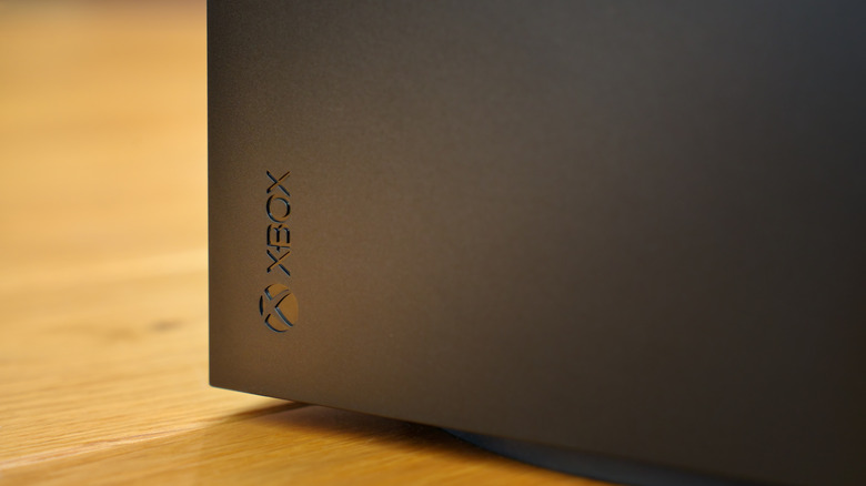 The Xbox logo on a black Xbox Series X sitting on a wooden surface.