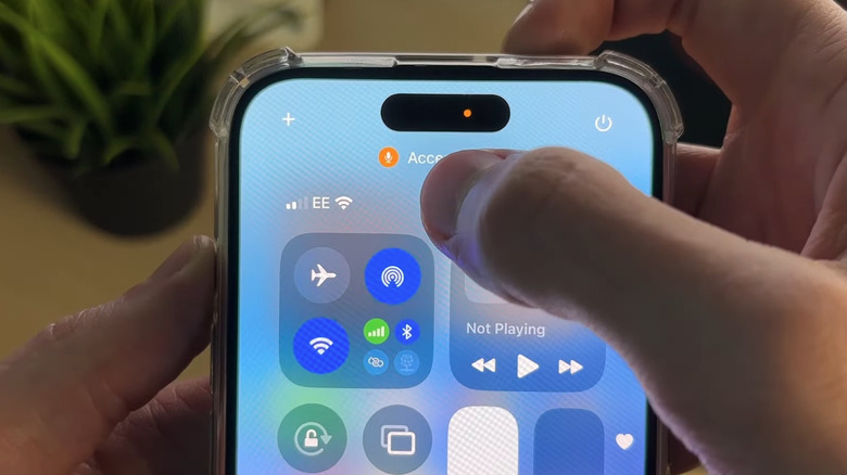 A person using an iPhone that's displaying the orange dot at the top of the screen.