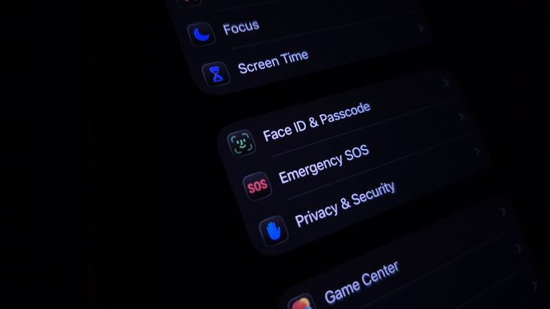An iPhone held in a dark room with the screen showing the "Face ID & Passcode" option, among other settings.