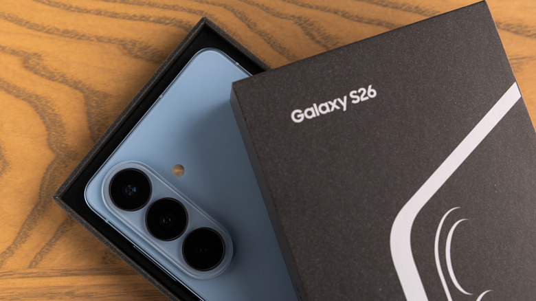 A light blue Samsung Galaxy S26 peaks out from its box as it sits on a wooden surface