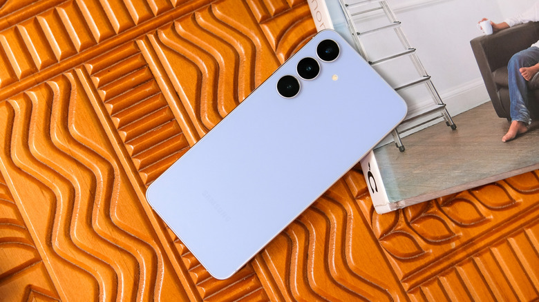 A light blue Samsung Galaxy S25 sits on a patterned wooden surface, one of the corners of the devices rests on top of a book