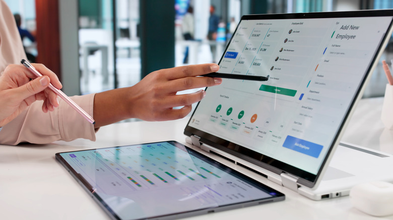 A person using a 2-in-1 laptop next to a tablet.
