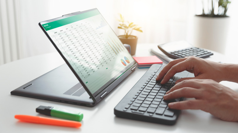 A person typing on a keyboard in front of a 2-in-1 laptop.