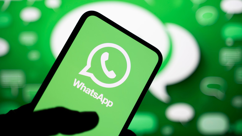 A hand holding a phone displaying the WhatsApp logo on a green background with white speech bubbles