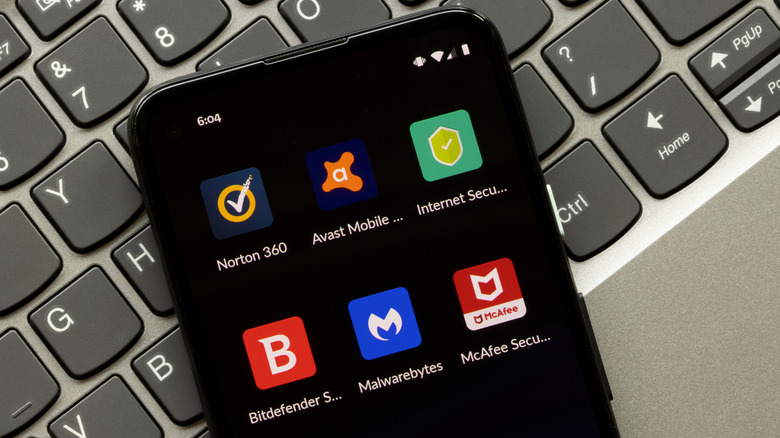 Android smartphone showing Norton, Avast, Internet Security, Bitdefender, Malwarebytes, and McAfee security apps placed on a laptop's keyboard