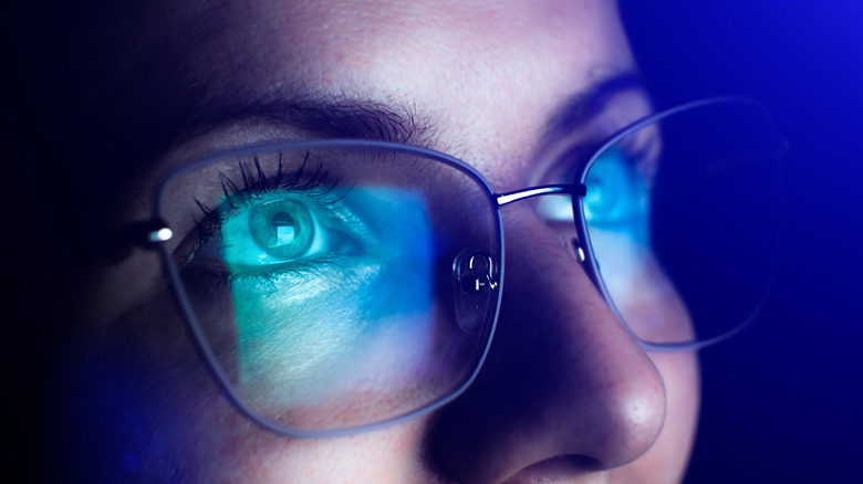 A woman looking at a computer screen with glasses on; blue light from the screen is being reflected in her glasses