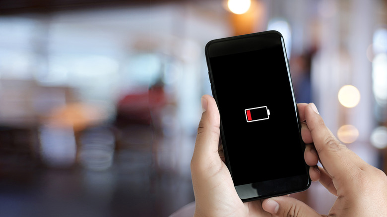 A person holding a phone in a busy room with a battery icon showing low battery