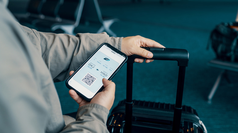 A person holding their phone displaying a plane ticket on the screen at an airport