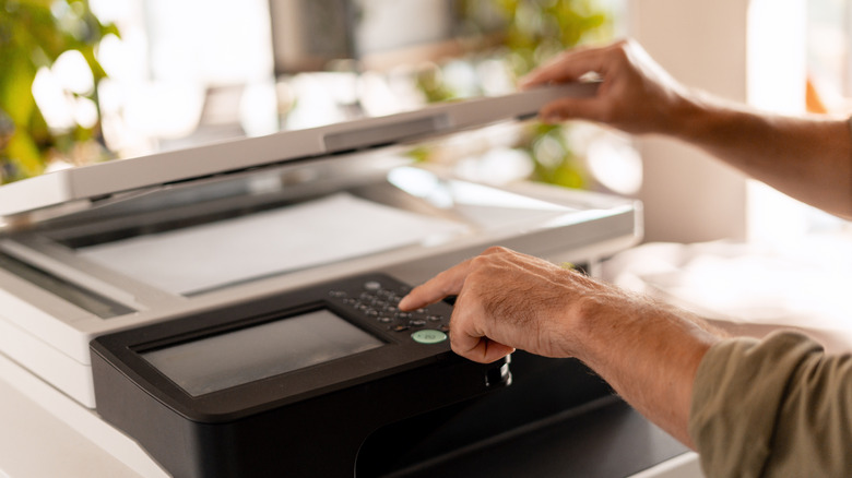 A person opening the lid of a scanner as they touch a button on the device.