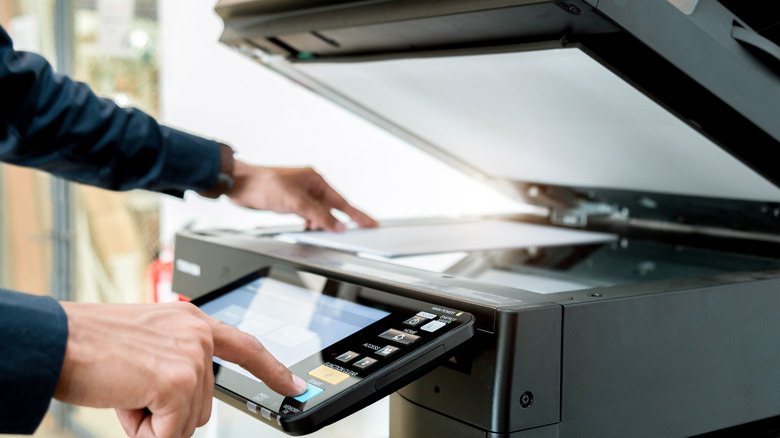 A person tapping a button on an office printer/scanner interface with the scanner lid open.