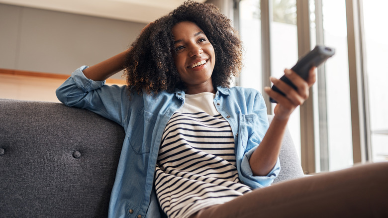 A woman sitting on a couch and holding a remote