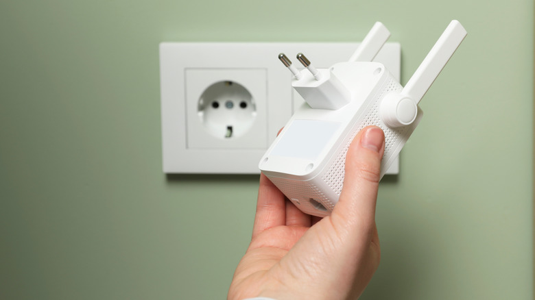 A person examining a Wi-Fi extender near a wall outlet