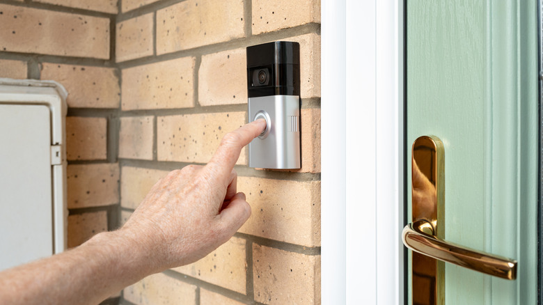 A hand reaching out to press the button on a Ring doorbell