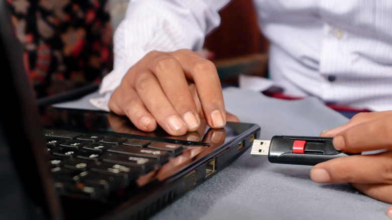 Someone plugging a USB-A flash drive into a laptop