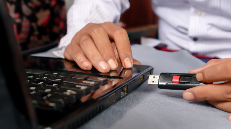 person connecting a black flash drive to a laptop
