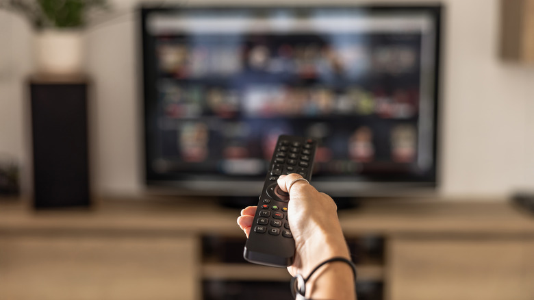 Aperson holding a remote and operating a smart TV.