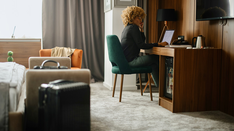 A person on a laptop sitting at a desk in a hotel room