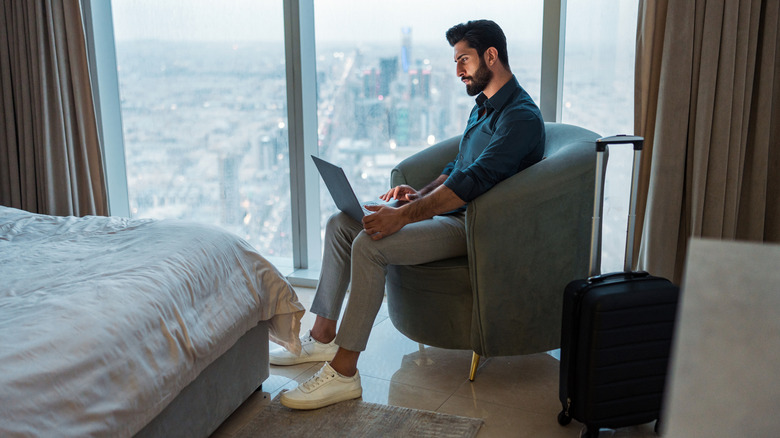 A person sitting by the window in a hotel room, while using a laptop