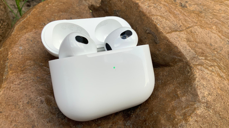 A pair of AirPods in their charging case, set against a rocky backdrop.
