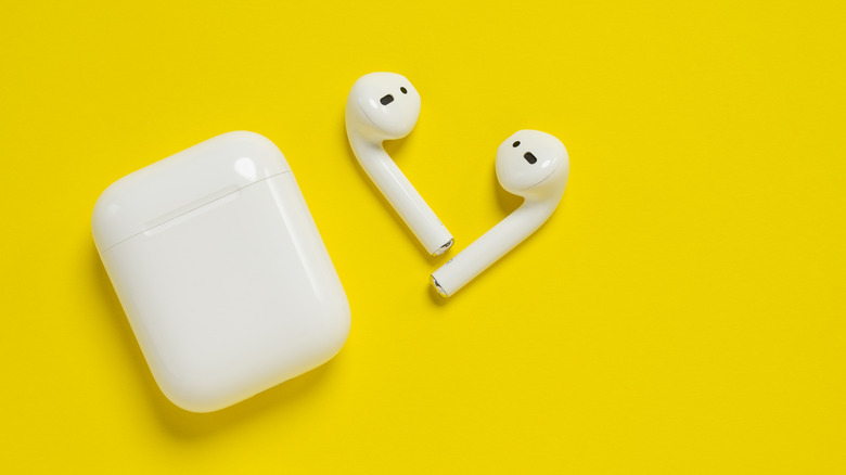 A pair of standard AirPods next to their charging case, set against a yellow background.