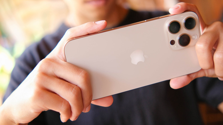 A closeup of an individual holding a white iPhone in between their hands, the device is held horizontally, suggesting the person may be taking a photo