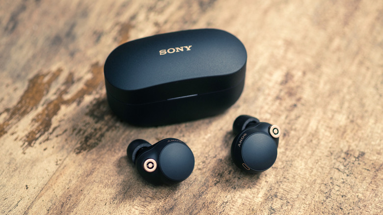 A pair of Sony wireless earbuds next to their charging case on a flat surface.