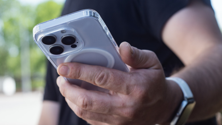 A closeup of an iPhone being held in an individual's left hand, the iPhone has a clear case