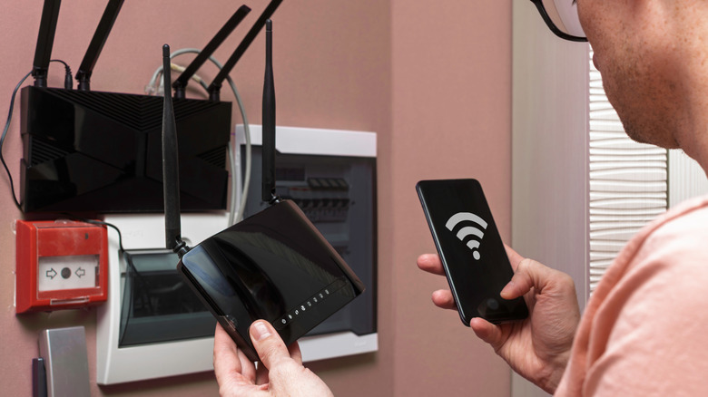 Man visibly troubleshooting a Wi-Fi router with a mobile phone and device in hand.