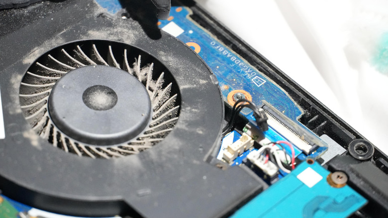 Dust-covered laptop cooling fan and internal components exposed during a hardware cleaning or repair.