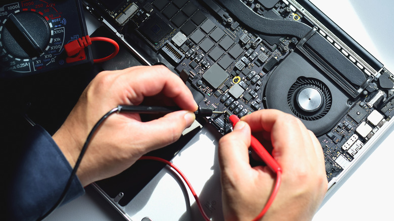 Technician testing an open laptop motherboard with a multimeter.
