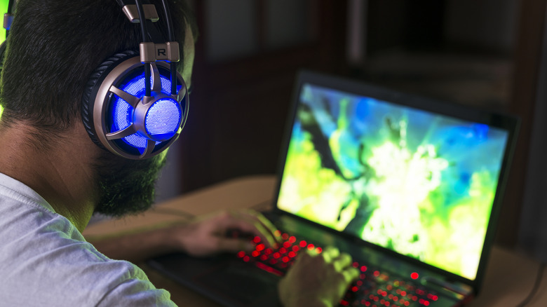 Person gaming on a laptop while wearing illuminated over-ear headphones.