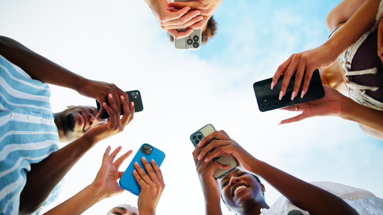 Multiple people using smartphones outside with the sun overhead.