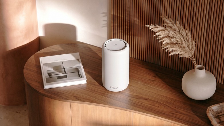 TP-Link's Deco 8 Ultra BN22000 mesh router on a table with a book and vase.