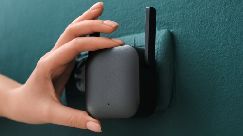 A person plugging a Wi-Fi extender in a wall outlet