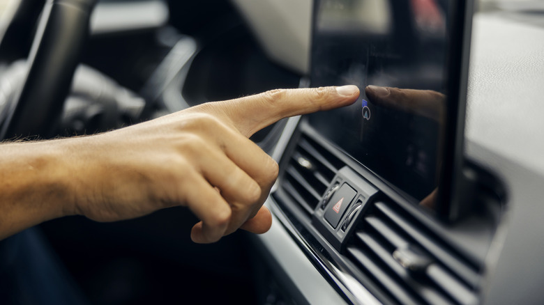 A person's hand pointing at a touchscreen in an electric vehicle