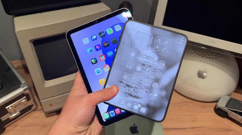 An iPhone Duo with iOS and an iPad mini with iPadOS being held in one hand in front of a desk