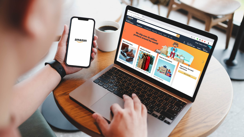 a person holding a phone with Amazon displayed on the screen next to a laptop showing the Amazon website