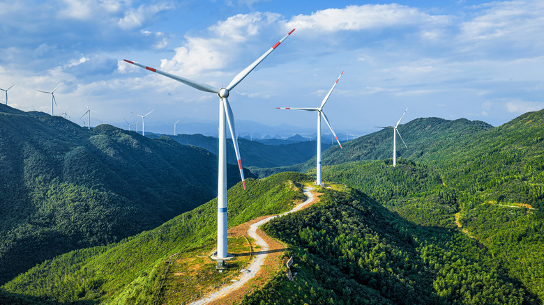 a wind farm built atop green mountains with a road