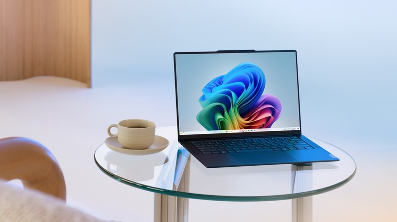 Windows laptop showing default wallpaper on coffee table next to cup of coffee