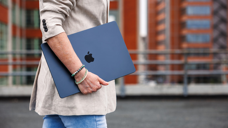 A person standing up holding a MacBook