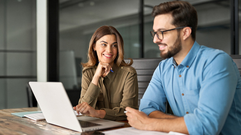 Two coworkers sitting in front of a laptop while talking with smiles on their faces